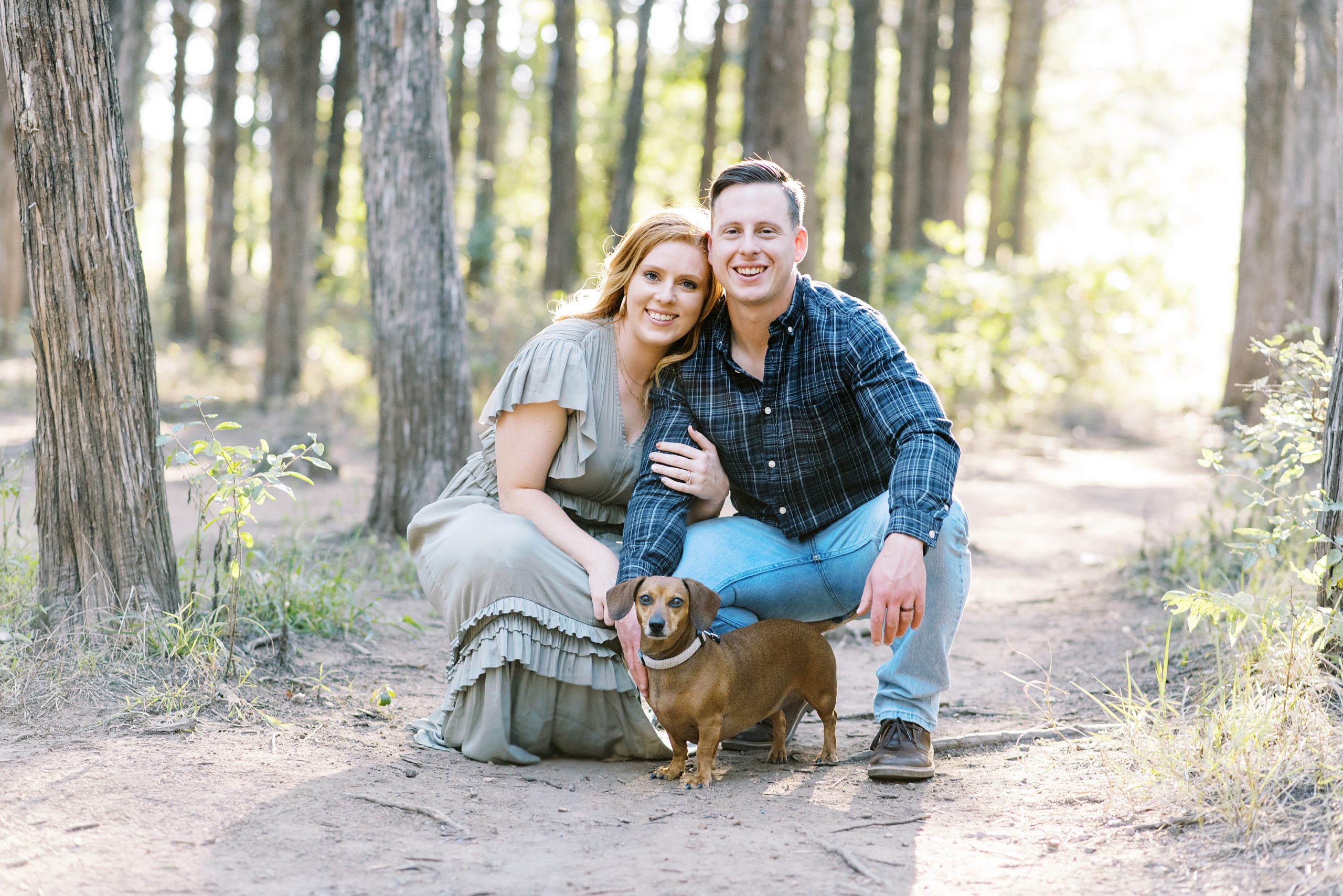 couple smiling with dog in forest